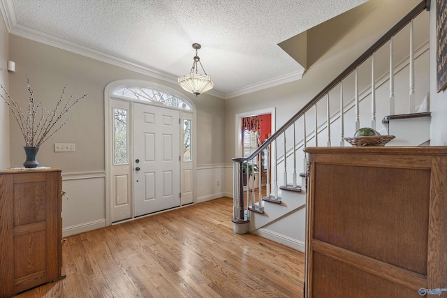 foyer featuring light wood finished floors, crown molding, stairs, and a textured ceiling