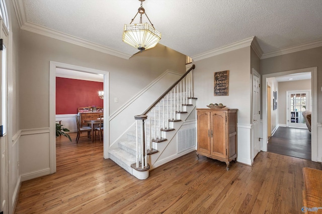 staircase featuring crown molding, a textured ceiling, and wood finished floors