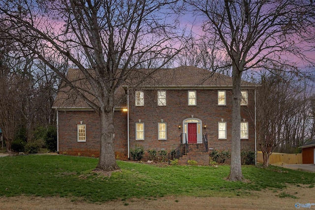 colonial-style house featuring brick siding, a yard, and fence