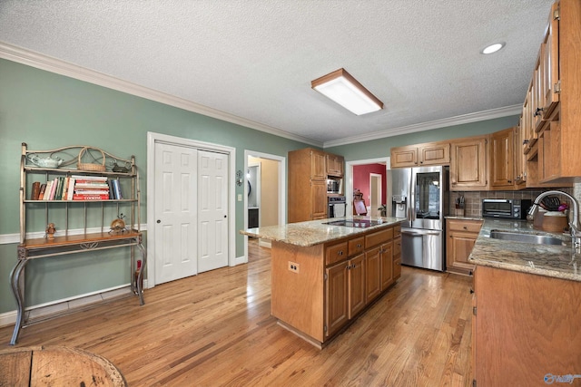 kitchen with light wood finished floors, light stone counters, a kitchen island with sink, stainless steel appliances, and a sink