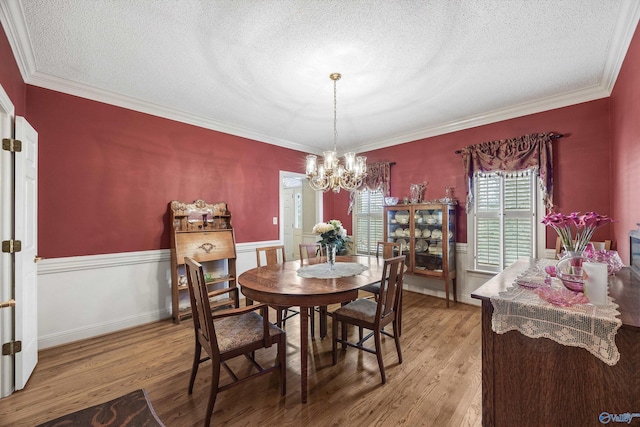 dining space featuring light wood finished floors, ornamental molding, wainscoting, a textured ceiling, and a chandelier