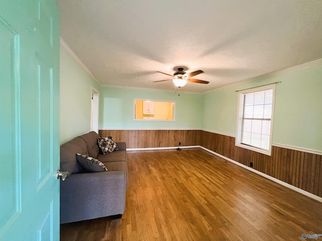 unfurnished room with wood finished floors, wainscoting, ornamental molding, ceiling fan, and a textured ceiling