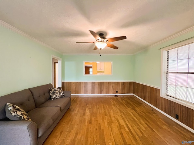 living area with wood finished floors, ceiling fan, a wainscoted wall, ornamental molding, and wood walls