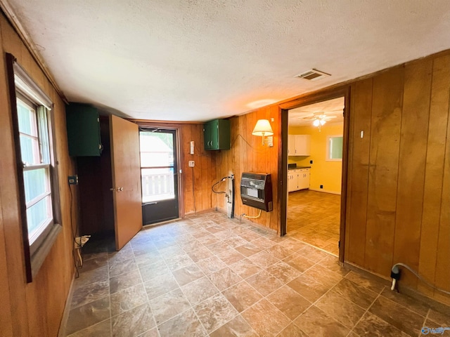 empty room with heating unit, wooden walls, plenty of natural light, a textured ceiling, and stone finish flooring