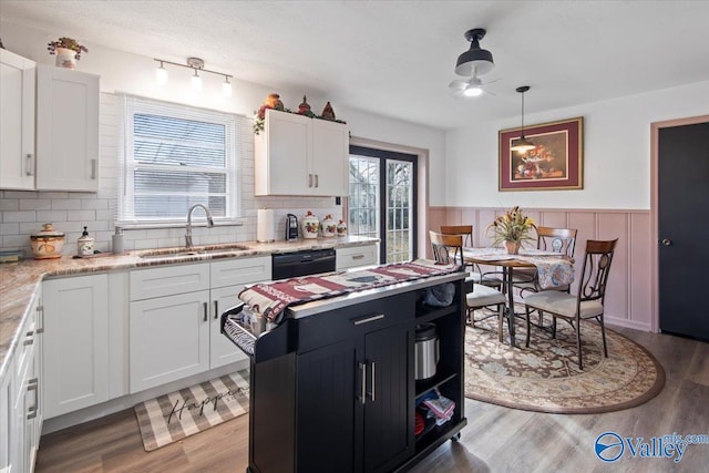 kitchen featuring sink, white cabinetry, hanging light fixtures, light hardwood / wood-style flooring, and black dishwasher