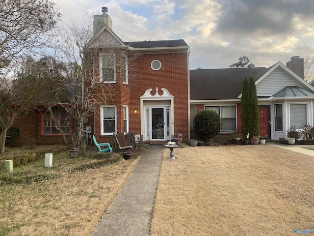 view of front of property with a front yard, brick siding, and a chimney