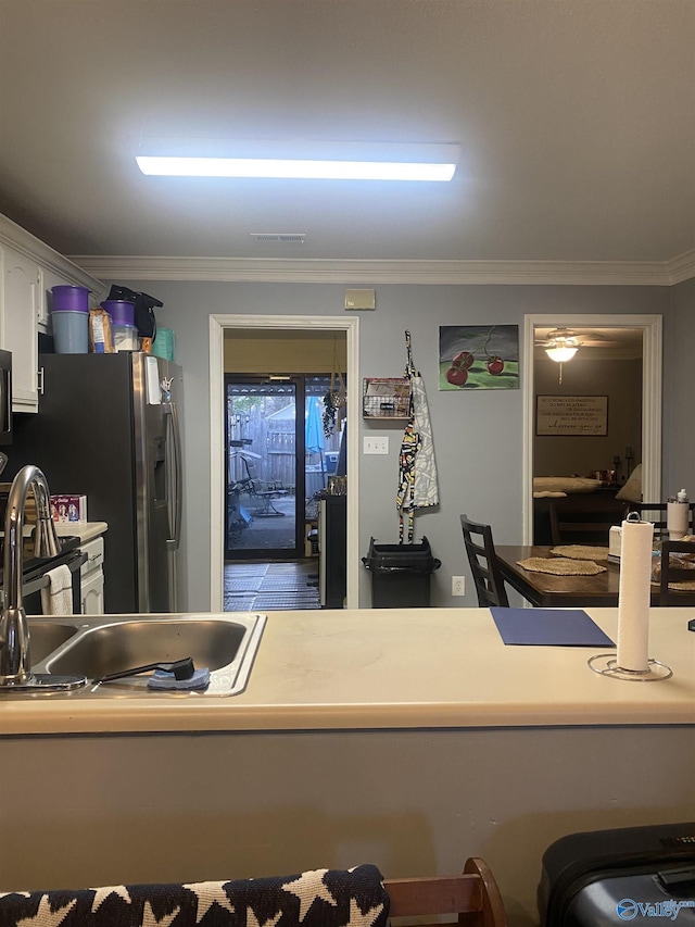 kitchen with white cabinetry, sink, stainless steel fridge, and crown molding