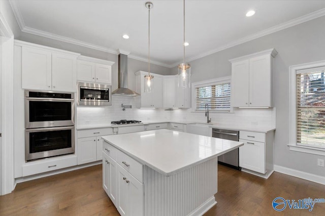 kitchen featuring appliances with stainless steel finishes, wall chimney exhaust hood, sink, a center island, and white cabinetry