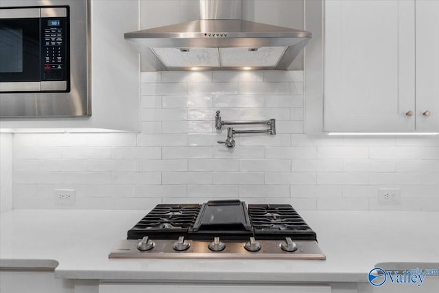 kitchen featuring white cabinets, wall chimney exhaust hood, decorative backsplash, and appliances with stainless steel finishes