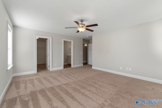 unfurnished bedroom featuring ensuite bath, a spacious closet, ceiling fan, light colored carpet, and a closet