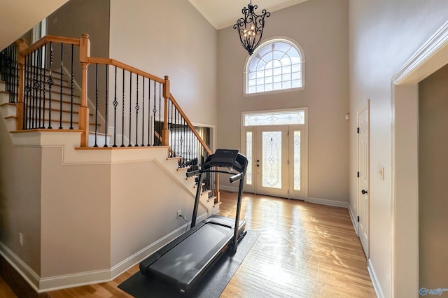 workout room featuring light hardwood / wood-style flooring, a towering ceiling, and a notable chandelier