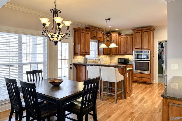 dining area featuring light wood-type flooring, a healthy amount of sunlight, a notable chandelier, and ornamental molding