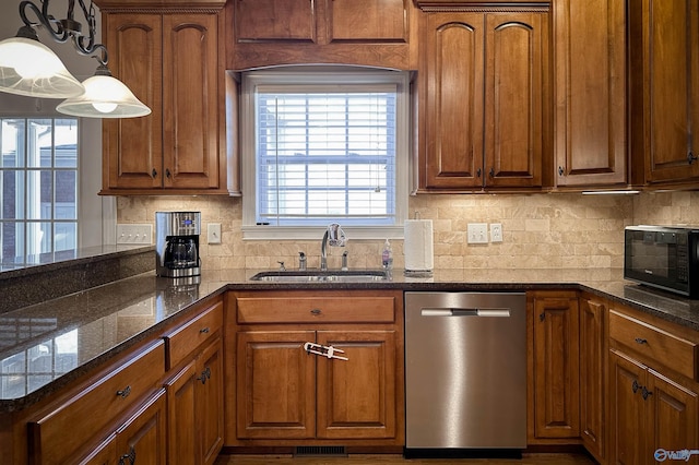 kitchen with pendant lighting, dishwasher, dark stone counters, sink, and backsplash