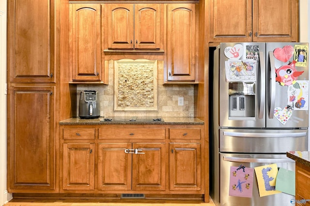 kitchen featuring decorative backsplash, stainless steel fridge, black electric stovetop, and dark stone counters