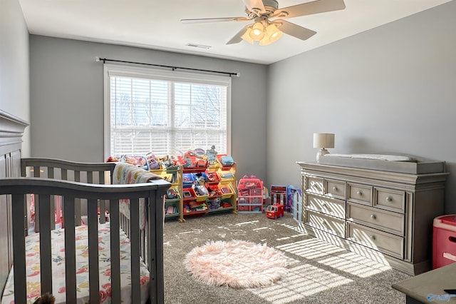 carpeted bedroom with ceiling fan and a nursery area