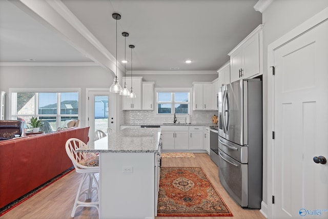 kitchen featuring open floor plan, light wood-type flooring, stainless steel appliances, white cabinetry, and a sink