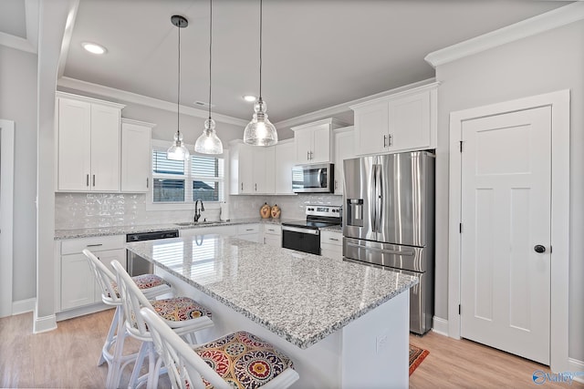 kitchen featuring a sink, ornamental molding, stainless steel appliances, white cabinets, and a kitchen bar