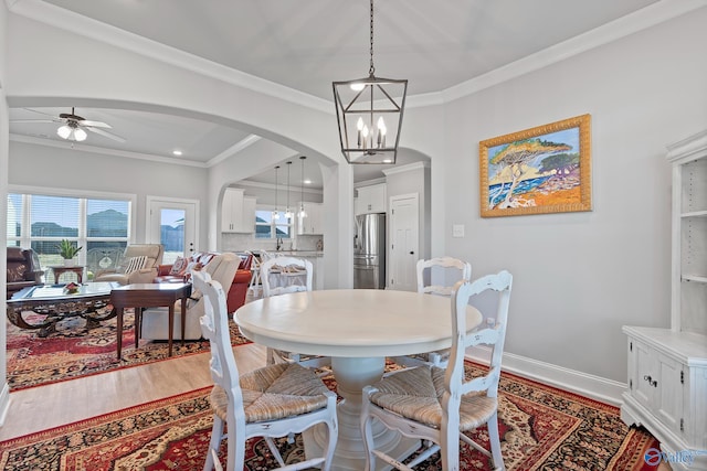 dining space with crown molding, baseboards, arched walkways, and light wood-type flooring