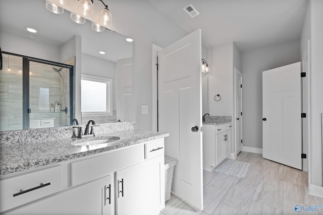 bathroom featuring visible vents, two vanities, a sink, a shower stall, and baseboards