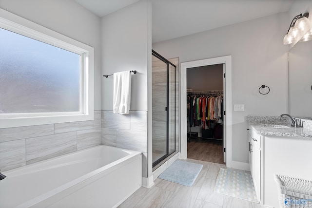 bathroom featuring a walk in closet, vanity, a shower stall, and a garden tub