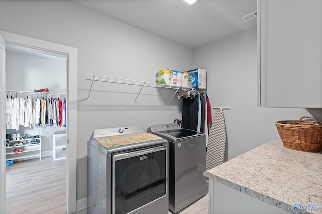 clothes washing area featuring light wood finished floors, visible vents, baseboards, washing machine and dryer, and laundry area