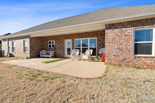 rear view of house featuring brick siding, a shingled roof, central AC unit, a lawn, and a patio area