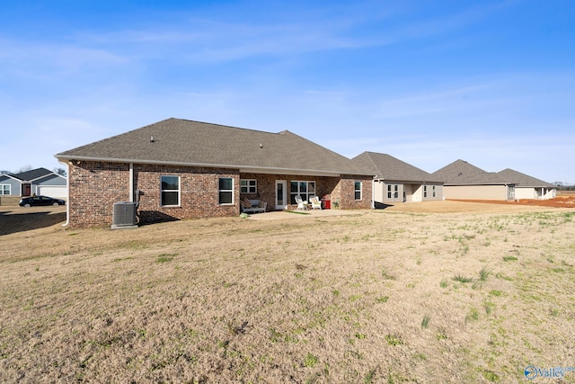 rear view of property featuring a yard, a shingled roof, brick siding, central AC unit, and a patio area