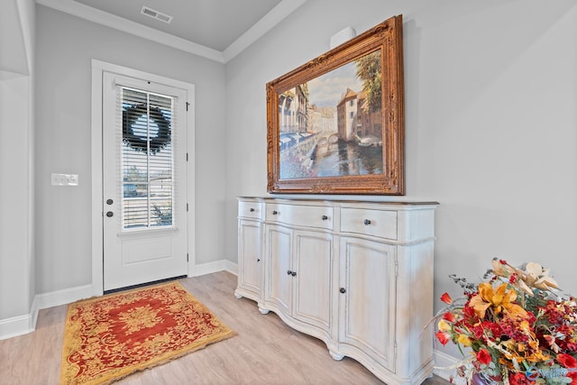 doorway to outside featuring light wood finished floors, visible vents, baseboards, and ornamental molding