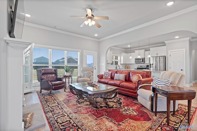 living room featuring ornamental molding, visible vents, arched walkways, and light wood-type flooring