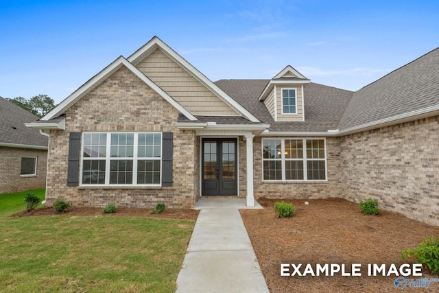 view of front of house with brick siding, a front yard, roof with shingles, and french doors
