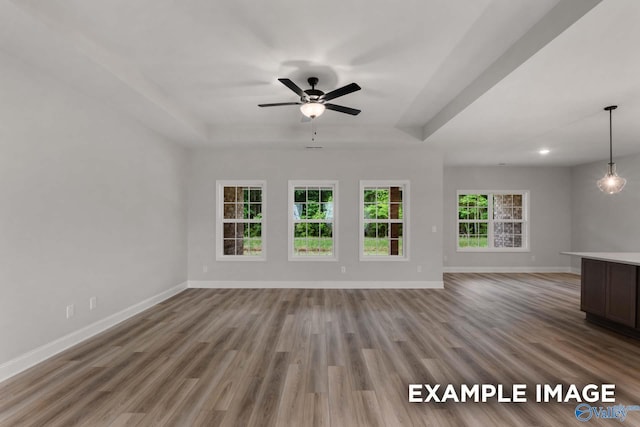 unfurnished living room with ceiling fan, baseboards, wood finished floors, and a raised ceiling