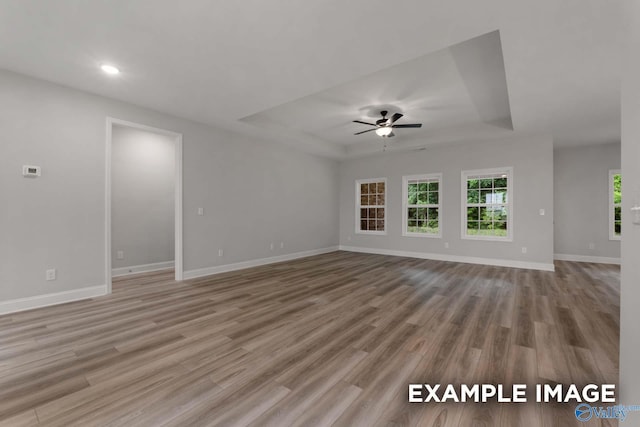 unfurnished living room featuring baseboards, recessed lighting, a tray ceiling, ceiling fan, and wood finished floors