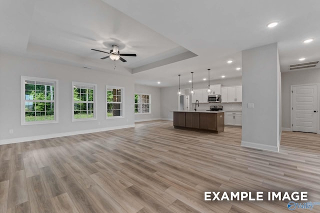 unfurnished living room featuring a wealth of natural light, recessed lighting, a tray ceiling, and a sink