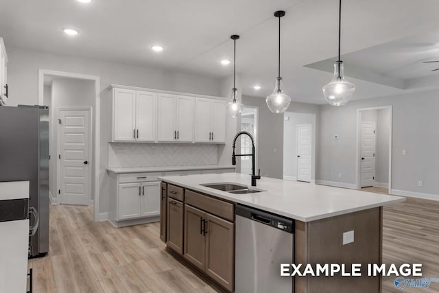 kitchen featuring tasteful backsplash, white cabinets, appliances with stainless steel finishes, light wood finished floors, and a sink