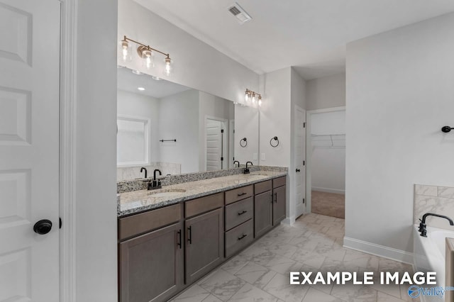 full bath with double vanity, a bathing tub, marble finish floor, and a sink
