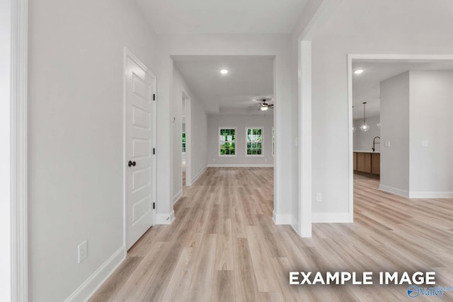 hall featuring recessed lighting, light wood finished floors, baseboards, and a sink
