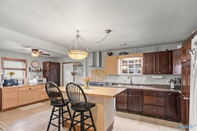 kitchen with wall chimney range hood, a center island, sink, and light tile patterned floors