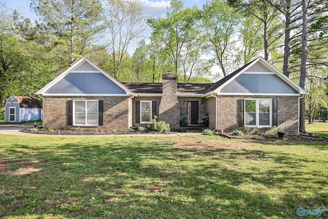 view of front of house featuring an outbuilding, a chimney, a storage unit, brick siding, and a front lawn