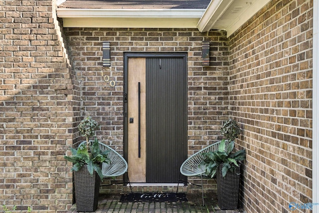 view of exterior entry featuring brick siding, elevator, and a shingled roof