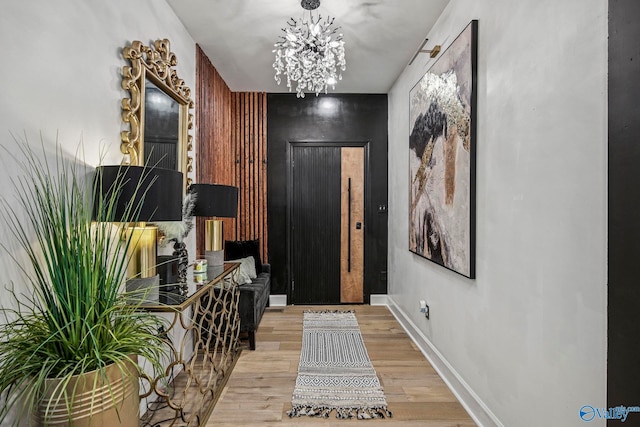 hallway featuring wood finished floors, an inviting chandelier, baseboards, and an accent wall