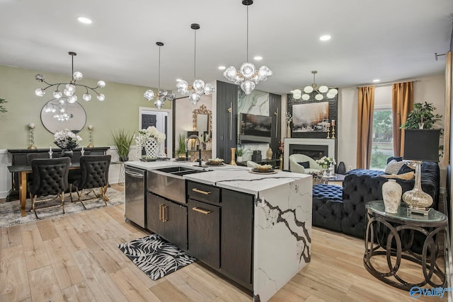 kitchen featuring a notable chandelier, open floor plan, a kitchen island with sink, light wood finished floors, and a sink