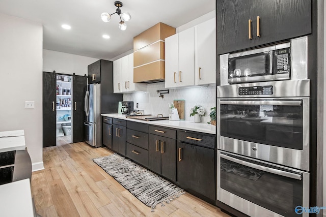 kitchen with tasteful backsplash, white cabinets, light countertops, light wood-type flooring, and stainless steel appliances