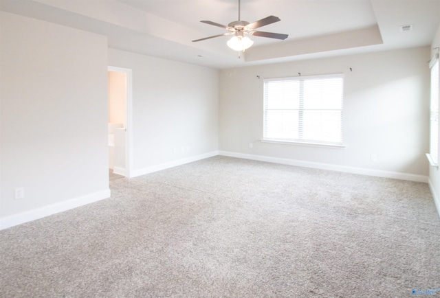 empty room with a tray ceiling, carpet floors, and ceiling fan