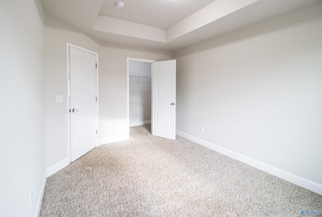 unfurnished bedroom with light carpet, a closet, and a raised ceiling