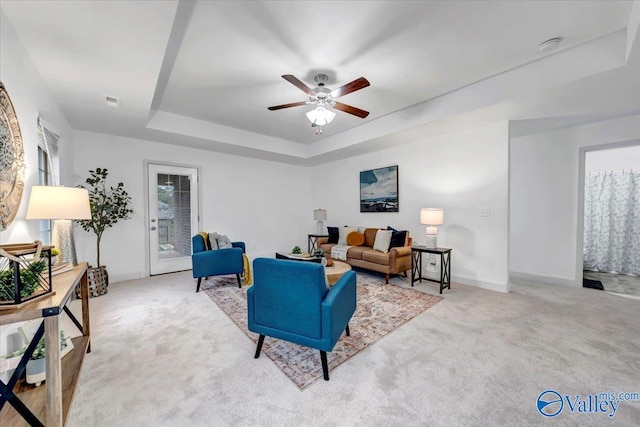 living room with a raised ceiling, light carpet, and ceiling fan