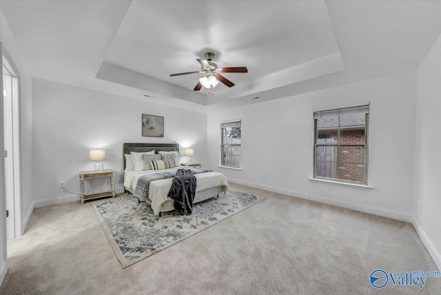 carpeted bedroom with ceiling fan, a tray ceiling, and multiple windows