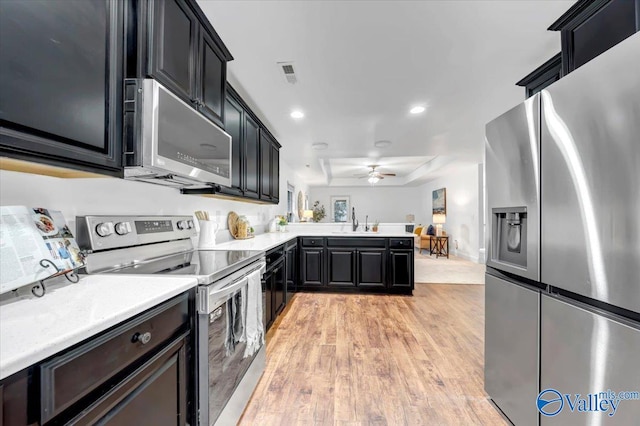 kitchen featuring ceiling fan, sink, stainless steel appliances, kitchen peninsula, and light wood-type flooring