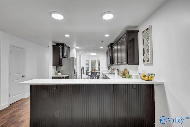 kitchen with dark wood-type flooring, sink, kitchen peninsula, a breakfast bar area, and stainless steel appliances