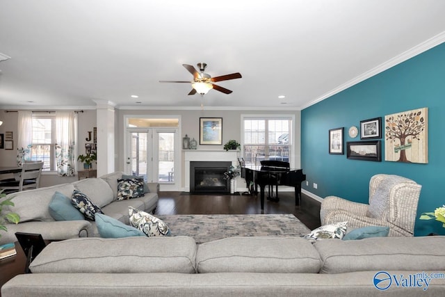 living room featuring baseboards, dark wood-type flooring, a glass covered fireplace, and crown molding