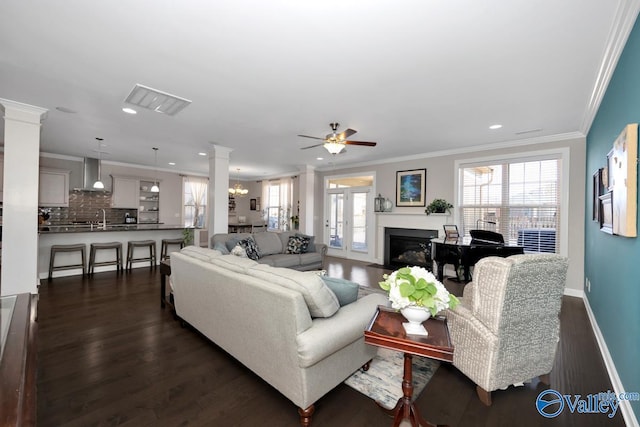 living area featuring dark wood-type flooring, a glass covered fireplace, crown molding, and ornate columns